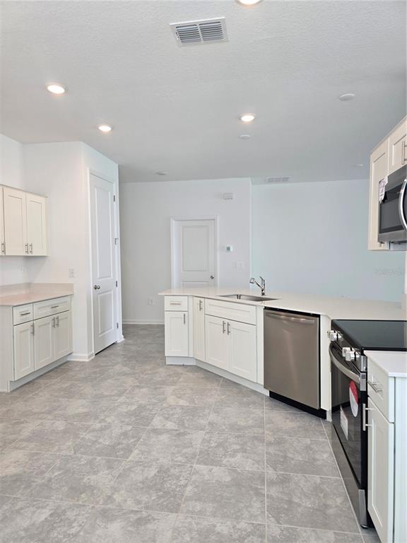 A kitchen with white cabinets, stainless steel appliances, and gray tile flooring — 1767 FOREMAN ROAD, EAGLE LAKE, FL