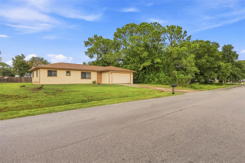 A single-story house with tan siding and an attached two-car garage sits on a lawn — 709 CUXHAVEN STREET NW, PALM BAY, FL