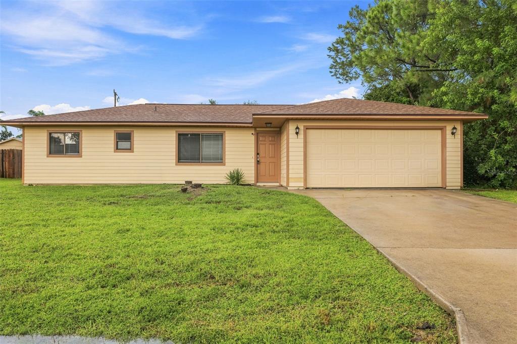 A single-story house with tan siding, a brown roof, and an attached two-car garage — 709 CUXHAVEN STREET NW, PALM BAY, FL