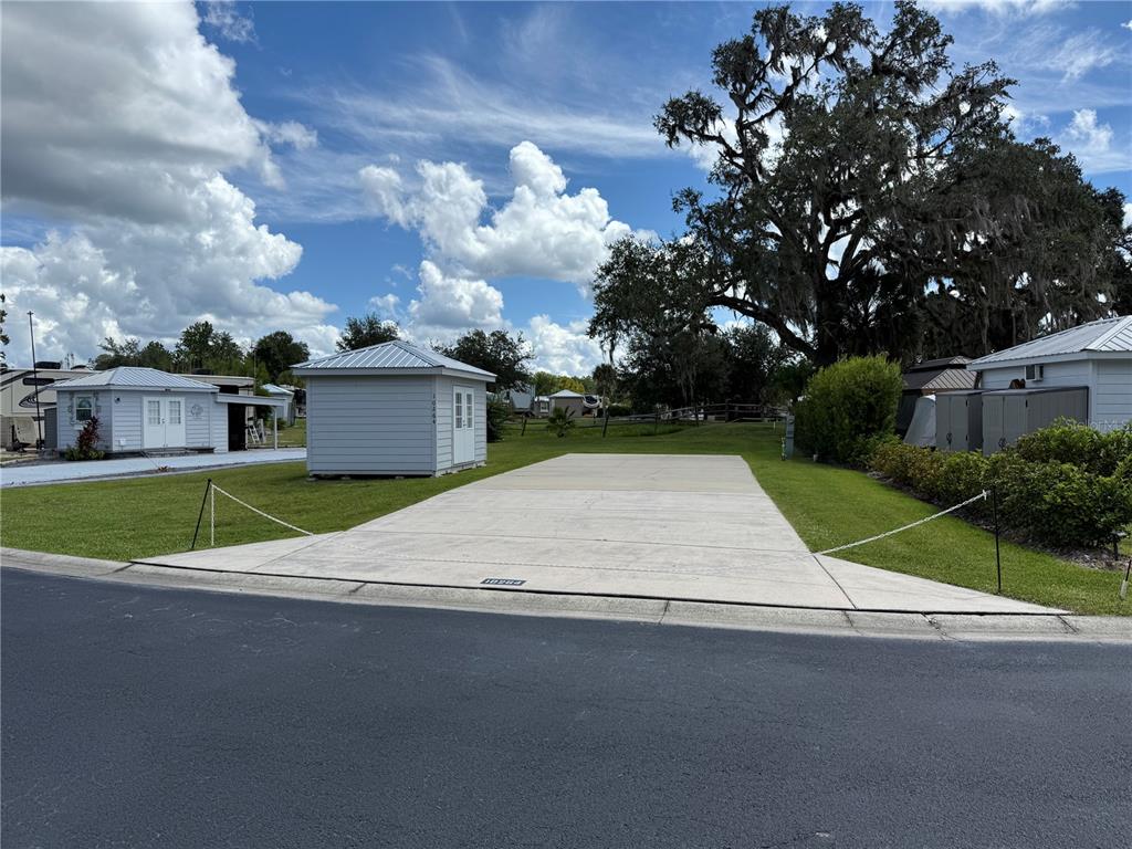 A concrete driveway sits between a small shed and a grassy lot under a blue sky — 10264 NE 28TH LOOP, SILVER SPRINGS, FL