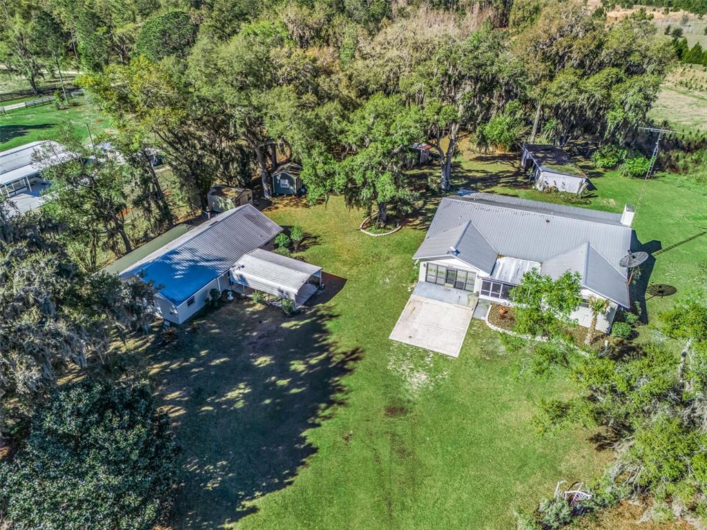 An aerial view shows two houses with metal roofs on a large, tree-filled grassy lot — 6350 NE 86TH AVENUE, BRONSON, FL