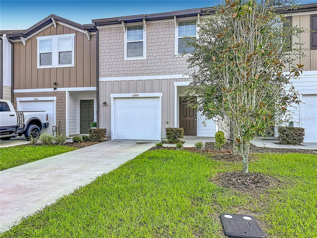 A two-story townhouse exterior features a concrete driveway, a garage, and a small front lawn — 6206 DAERR RIDGE STREET, ZEPHYRHILLS, FL