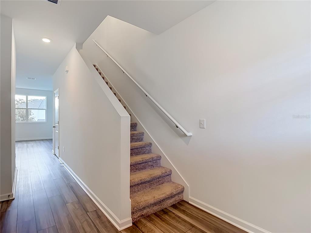 A carpeted staircase with a white handrail sits beside a hallway with wood-look flooring — 6206 DAERR RIDGE STREET, ZEPHYRHILLS, FL