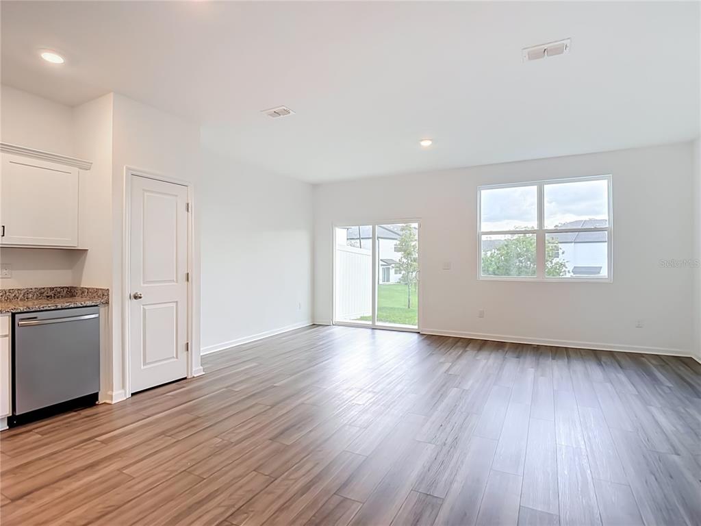 An open-concept room features wood-look flooring, a kitchen corner, a sliding glass door, and windows — 6206 DAERR RIDGE STREET, ZEPHYRHILLS, FL
