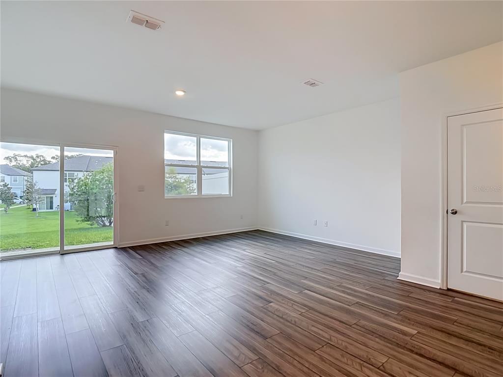 An empty room features dark wood-look flooring, white walls, a sliding glass door, and windows — 6206 DAERR RIDGE STREET, ZEPHYRHILLS, FL