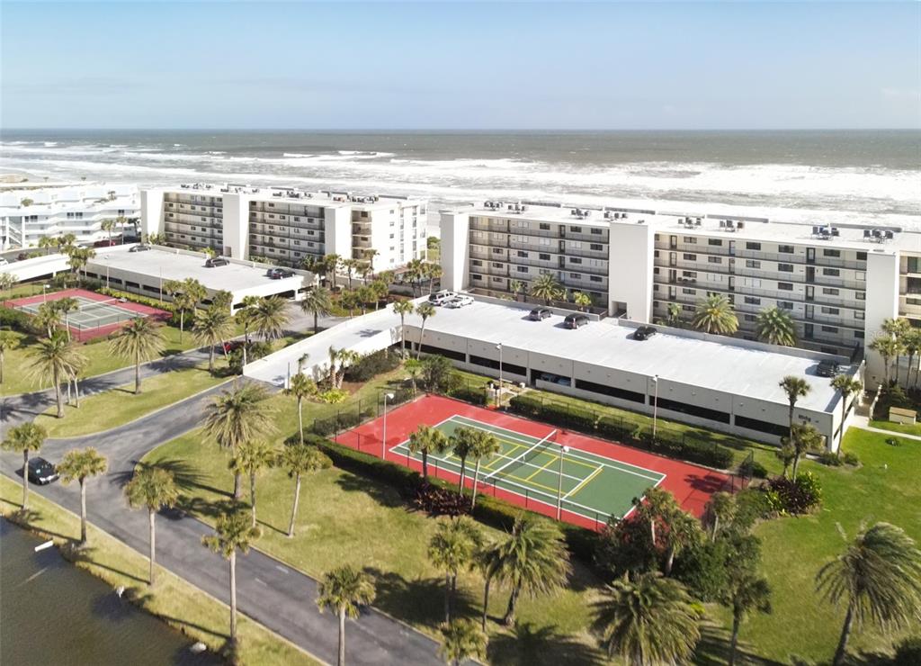 An aerial view shows two beachfront apartment buildings with parking garages and tennis courts — 7990 A1A S UNIT 404, ST AUGUSTINE, FL