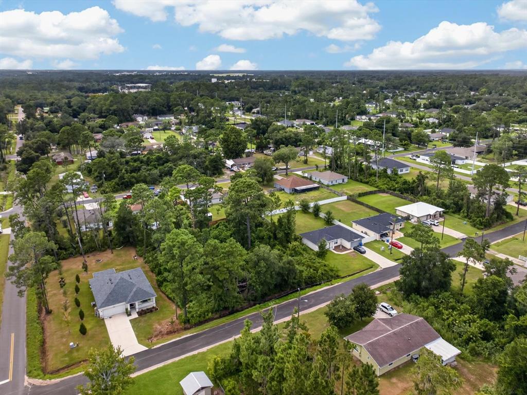 An aerial view shows a suburban neighborhood with single-family homes, paved streets, and wooded areas — 6TH AVENUE, DELAND, FL