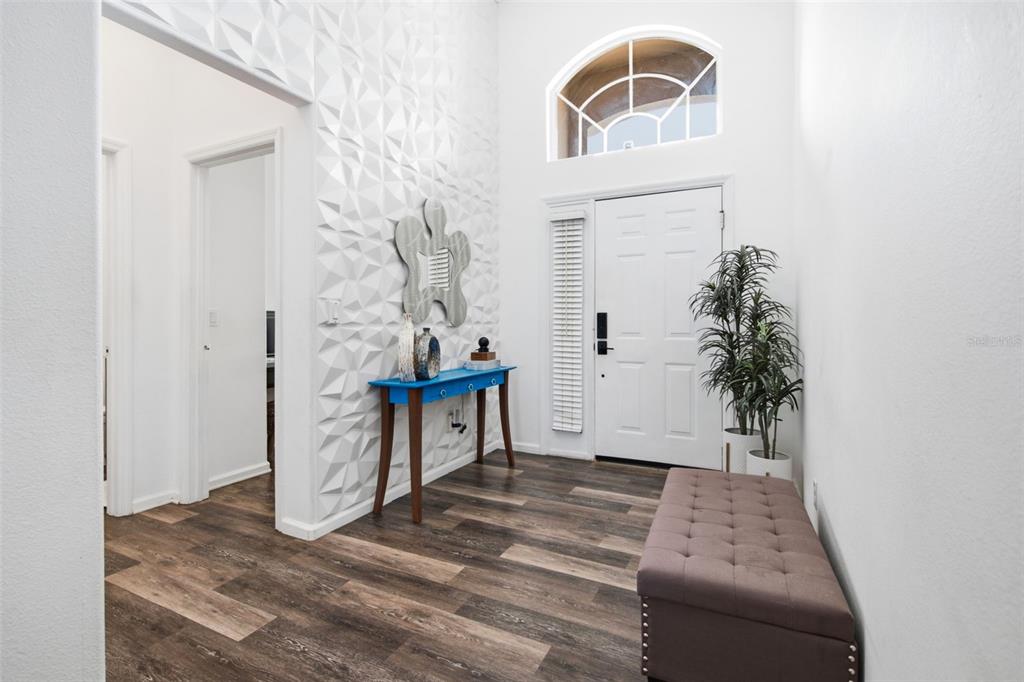 A bright entryway features a textured accent wall, a blue console table, and wood-look flooring — 6539 CHERRY GROVE CIRCLE, ORLANDO, FL