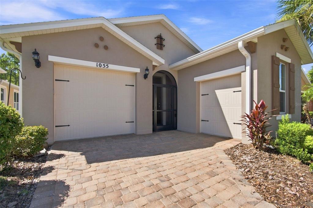 A beige house exterior features a two-car garage, a paved driveway, and a front entryway — 1055 HARBOR RIDGE DRIVE, KISSIMMEE, FL