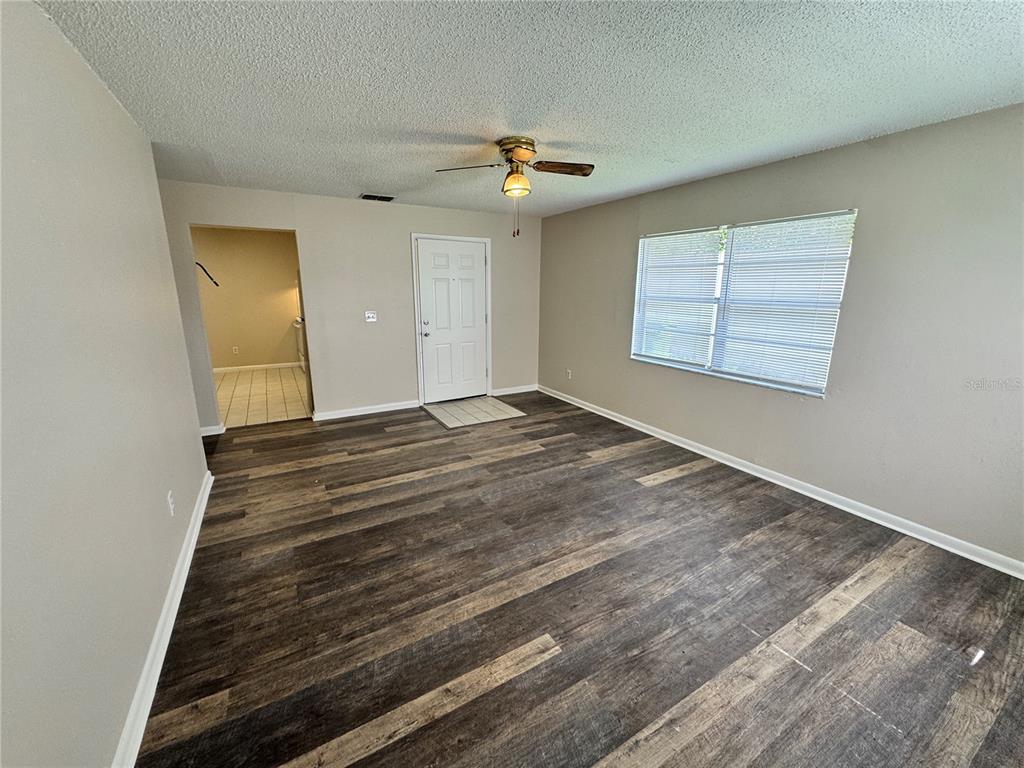 An empty living room features wood-look flooring, a ceiling fan, and a white entry door — 1001 CRAWFORD STREET Unit 1, LEESBURG, FL