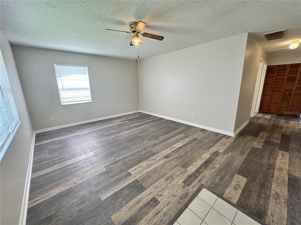 An empty room features gray wood-look flooring, light-colored walls, a ceiling fan, and a window — 1001 CRAWFORD STREET Unit 1, LEESBURG, FL