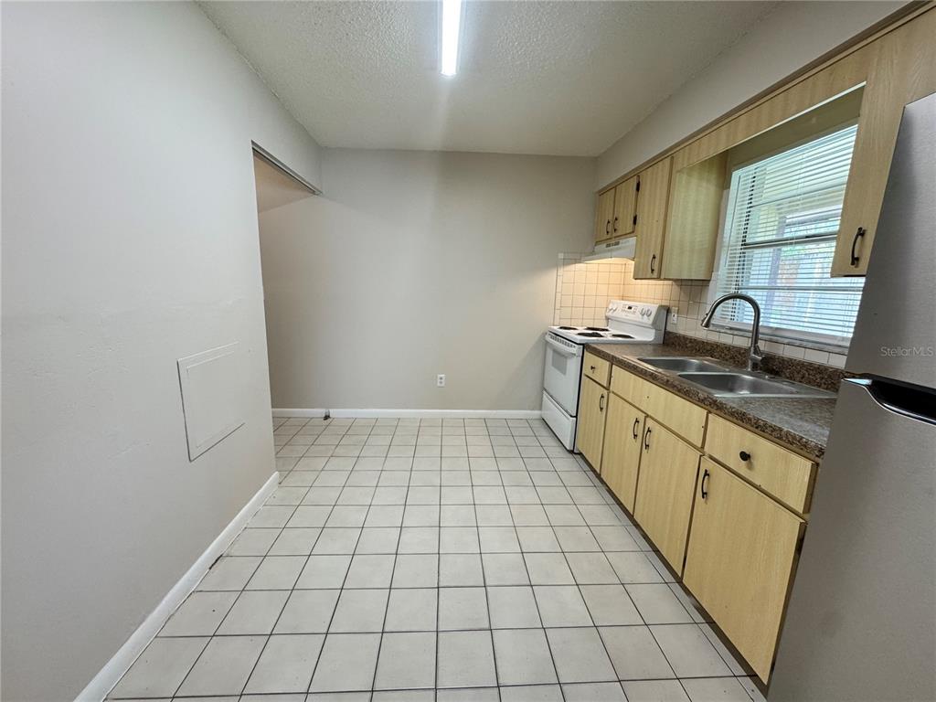 A kitchen features light wood cabinets, tiled flooring, a white stove, and a double sink — 1001 CRAWFORD STREET Unit 1, LEESBURG, FL