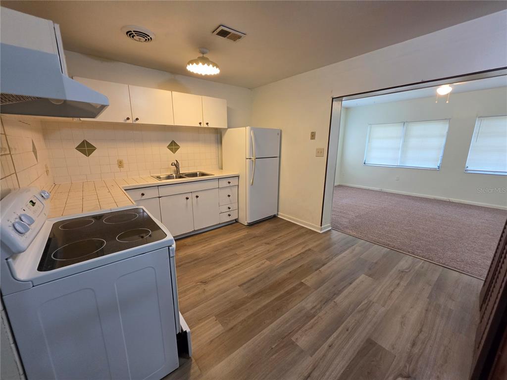 A kitchen with white cabinets, a white stove, and wood-look flooring opens to a carpeted room — 1103 N CRYSTAL TERRACE, PLANT CITY, FL