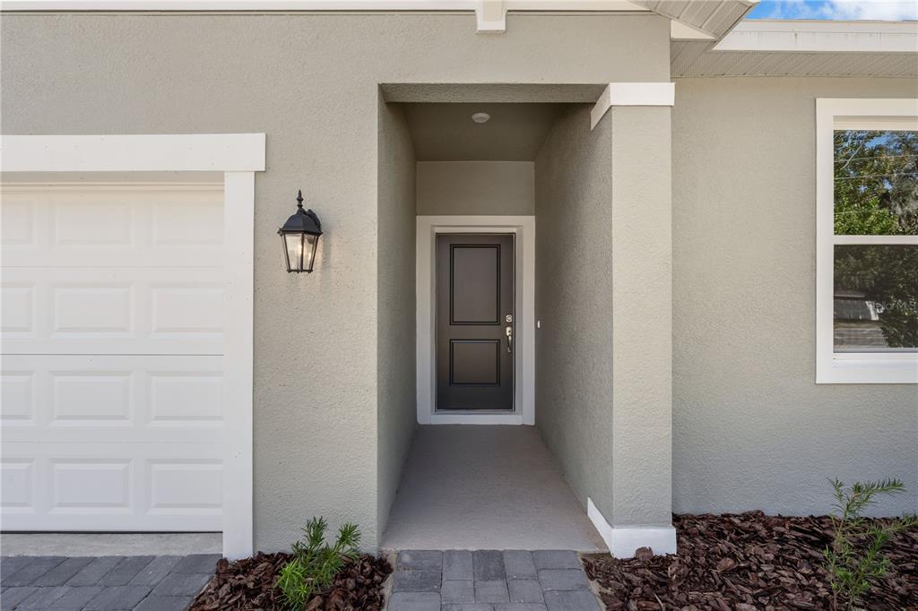 A view of a home exterior featuring a dark front door, garage, and paved walkway — 5812 CLIFFBOW LOOP, LEESBURG, FL