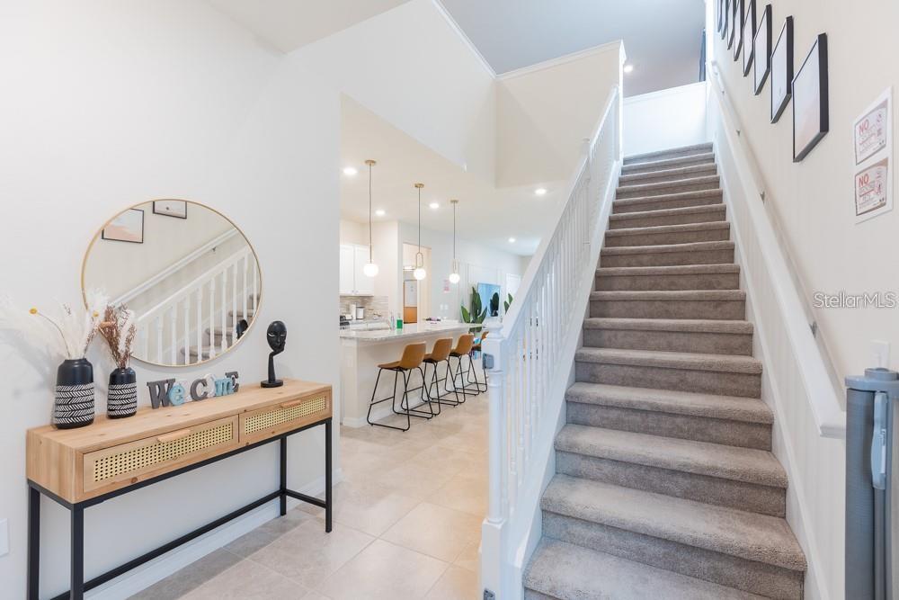 An entryway features a console table, a round mirror, and a carpeted staircase leading upstairs — 7215 OAKMOSS LOOP, DAVENPORT, FL