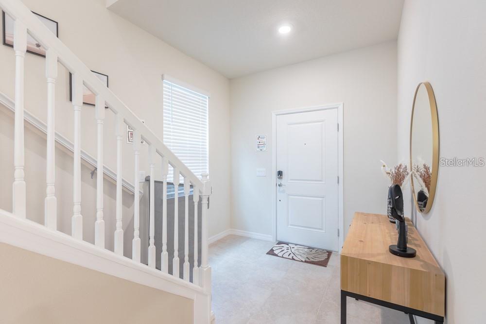 An entryway features a white staircase, a front door, a wood console table, and a mirror — 7215 OAKMOSS LOOP, DAVENPORT, FL