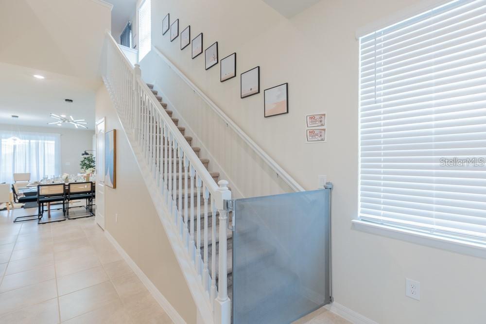 A staircase with a safety gate leads to an upper level in a bright home — 7215 OAKMOSS LOOP, DAVENPORT, FL