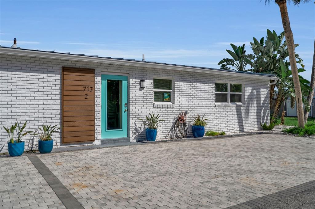 A white brick exterior features a teal front door, wood paneling, and a paved driveway — 713 SAINT JUDES DRIVE S UNIT 2, LONGBOAT KEY, FL