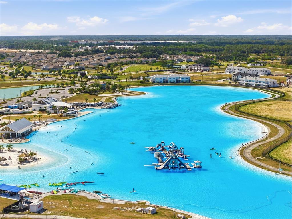 An aerial view shows a large turquoise lagoon with an inflatable water park and beach — 10770 TUPPER CAY DRIVE, SAN ANTONIO, FL