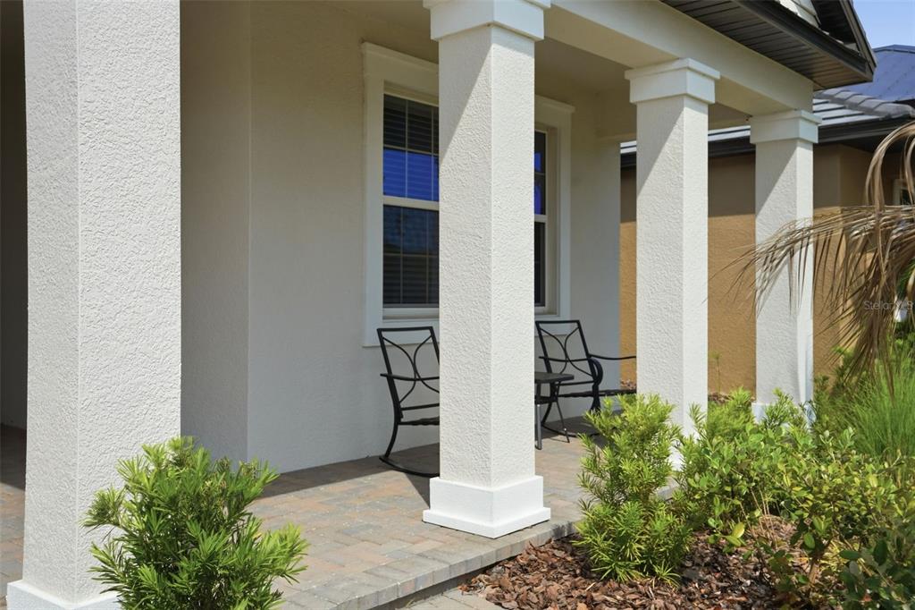 A covered front porch features white square columns, a paver floor, and two metal chairs — 10770 TUPPER CAY DRIVE, SAN ANTONIO, FL