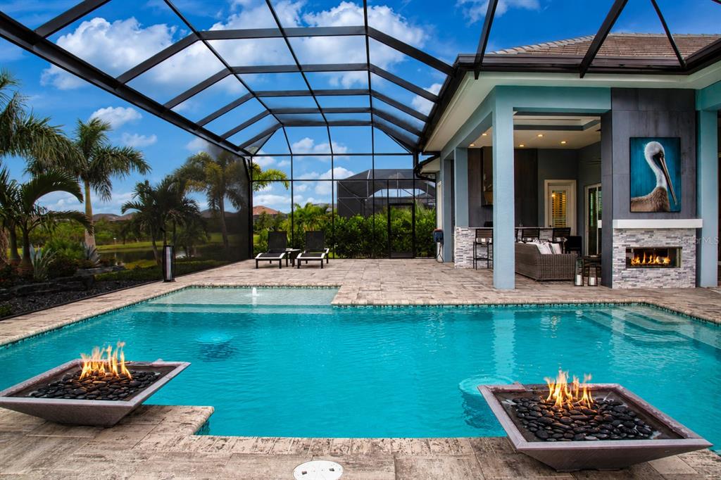 A swimming pool with two fire bowls sits on a patio under a screened enclosure — 7935 BOWSPIRIT WAY, BRADENTON, FL
