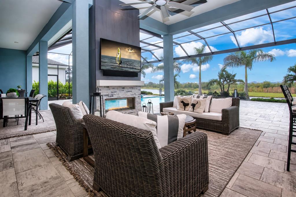 A covered outdoor patio features a fireplace, television, wicker furniture, and a screened-in pool area — 7935 BOWSPIRIT WAY, BRADENTON, FL