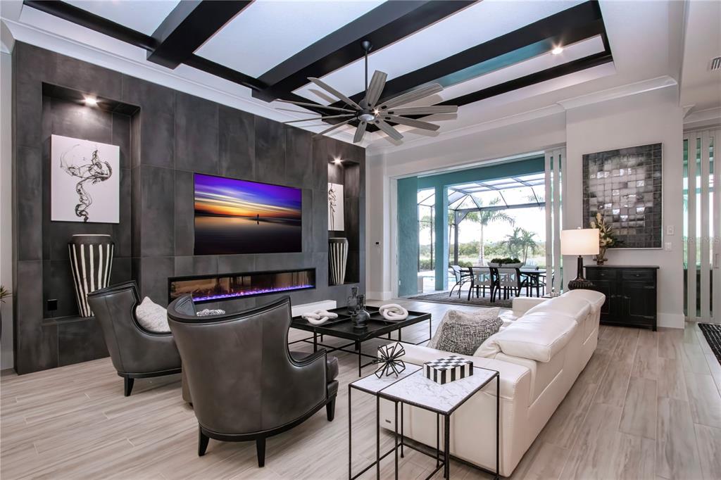 A modern living room features a dark tiled fireplace wall, coffered ceiling, and sliding glass doors — 7935 BOWSPIRIT WAY, BRADENTON, FL