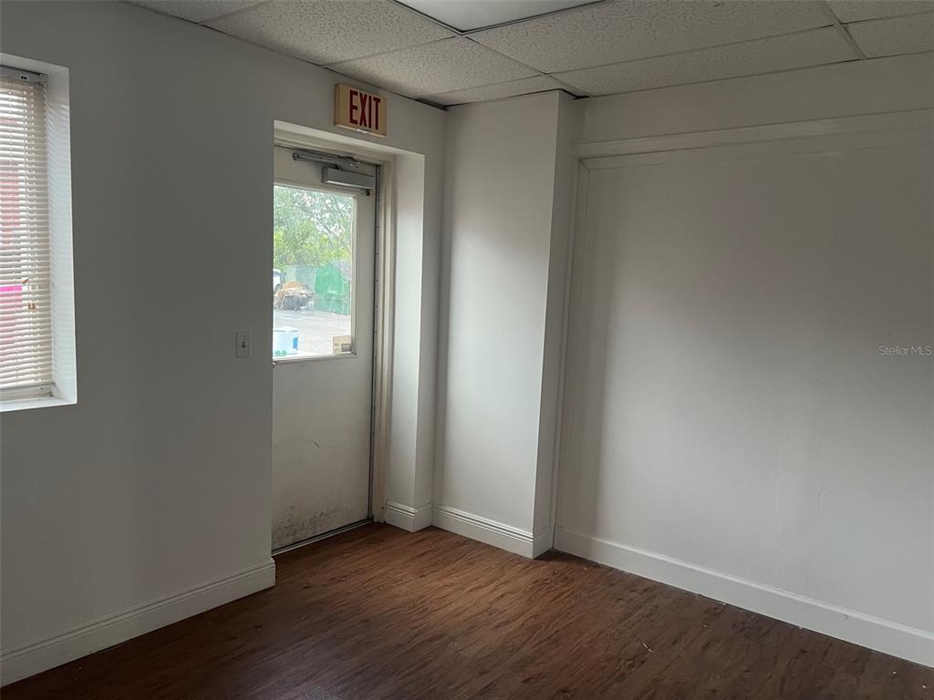 An interior room features white walls, wood-look flooring, a window with blinds, and an exit door — 2433 S 86TH STREET, TAMPA, FL