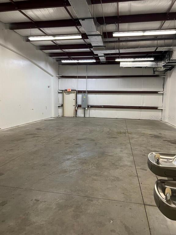 An empty industrial warehouse space features concrete floors, exposed ceiling beams, and a single door — 2433 S 86TH STREET, TAMPA, FL