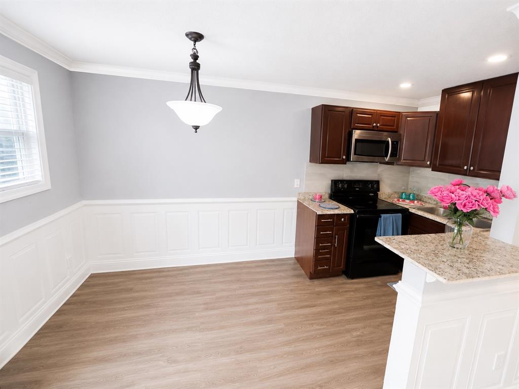 A dining area with wainscoting and wood-look flooring adjacent to a kitchen with dark cabinets — 4666 KEN KNIGHT DRIVE N, JACKSONVILLE, FL