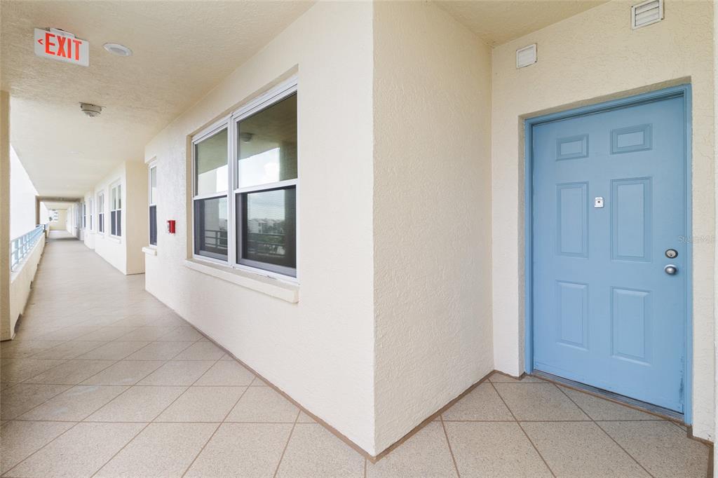 A light blue door sits at the end of a tiled outdoor apartment building walkway — 7974 SAILBOAT KEY BOULEVARD S UNIT 408, SOUTH PASADENA, FL