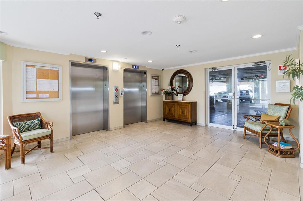 A lobby area features two elevators, tiled flooring, two wicker chairs, and a glass-paned exit — 7974 SAILBOAT KEY BOULEVARD S UNIT 408, SOUTH PASADENA, FL