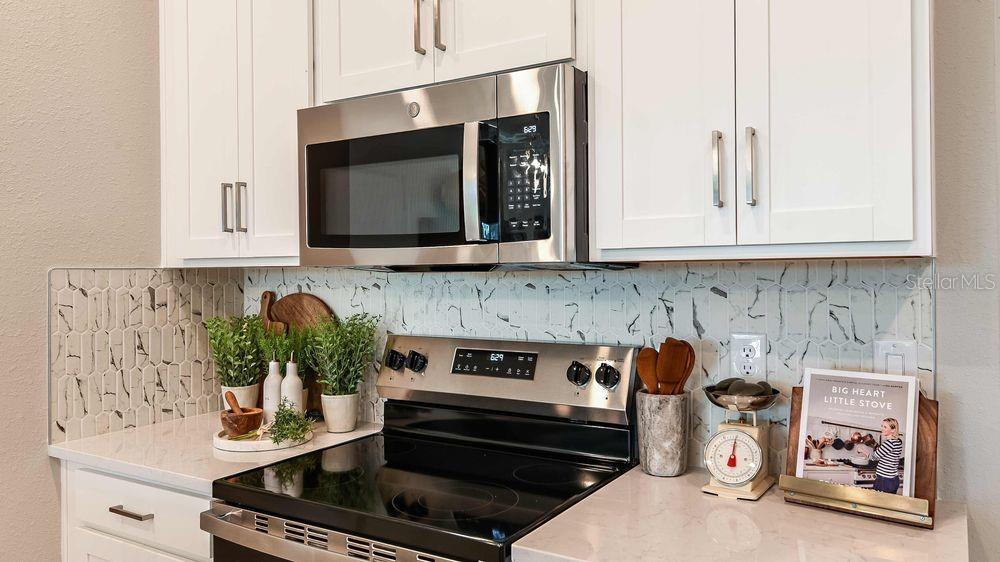 A kitchen features white cabinets, a stainless steel microwave, a glass-top stove, and marble-patterned backsplash — 25 GEOSAM DRIVE, PALM COAST, FL