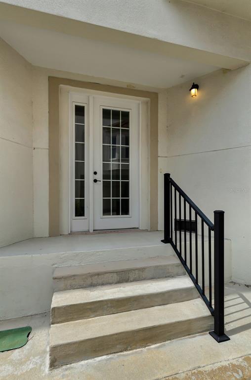 A white front door with a sidelight and black railing sits atop concrete steps — 1340 BAYSHORE BOULEVARD UNIT 304, DUNEDIN, FL