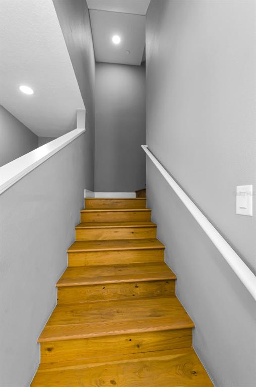 A staircase with wooden treads and white handrails leads upward between gray walls — 1340 BAYSHORE BOULEVARD UNIT 304, DUNEDIN, FL
