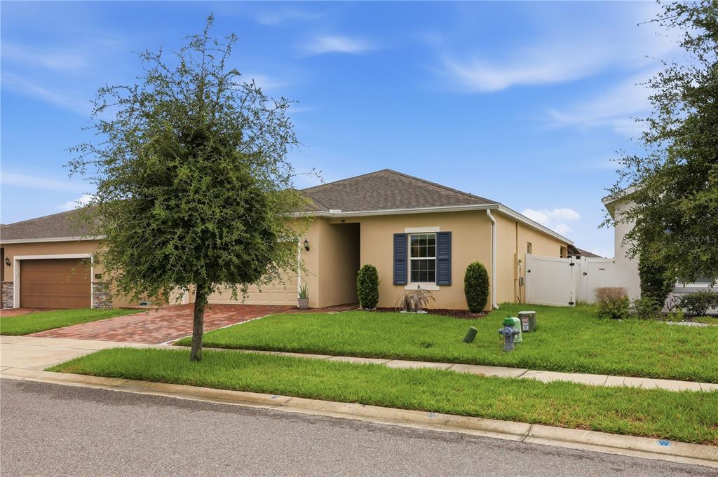 A single-story tan house with a brick driveway, a front tree, and a blue-shuttered window — 490 DISA DRIVE, DAVENPORT, FL