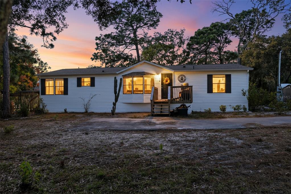 A single-story white house with black shutters and a front porch sits at dusk — 17539 EDWIN TERRACE, HUDSON, FL