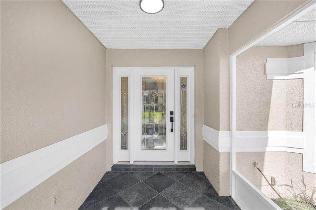 A covered entryway features a white front door with sidelights and dark tiled flooring — 6501 BORG STREET, LEESBURG, FL