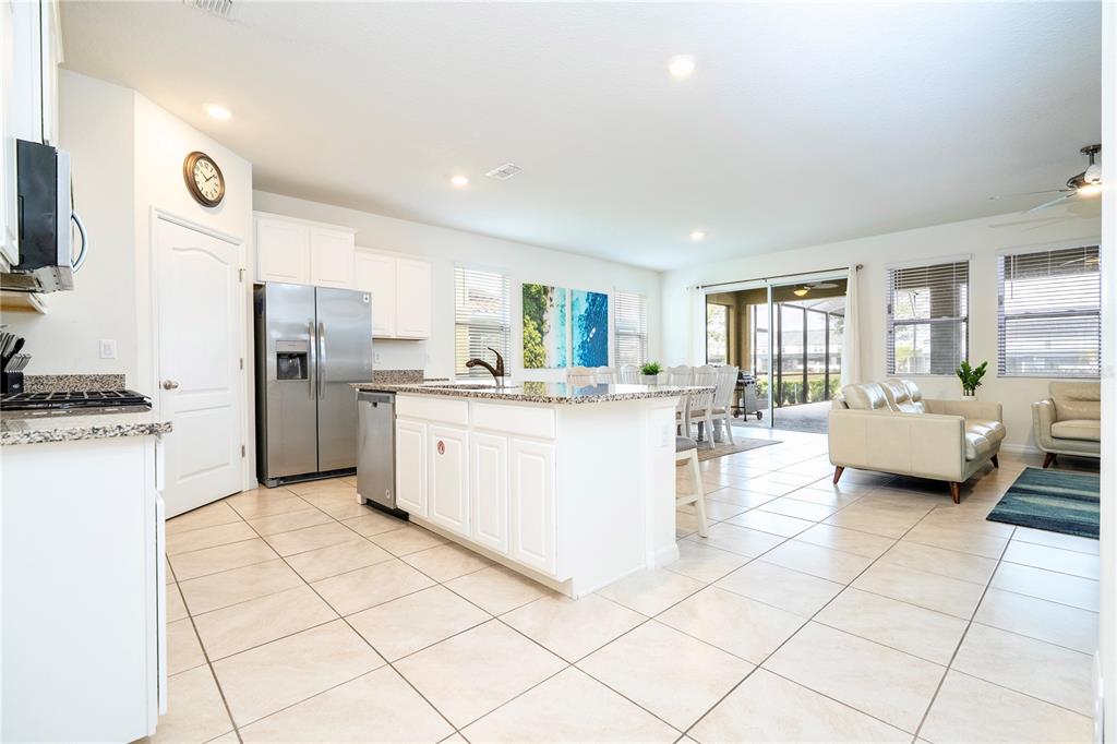A kitchen with white cabinets and granite countertops opens into a living and dining area — 7560 OAKMOSS LOOP, DAVENPORT, FL
