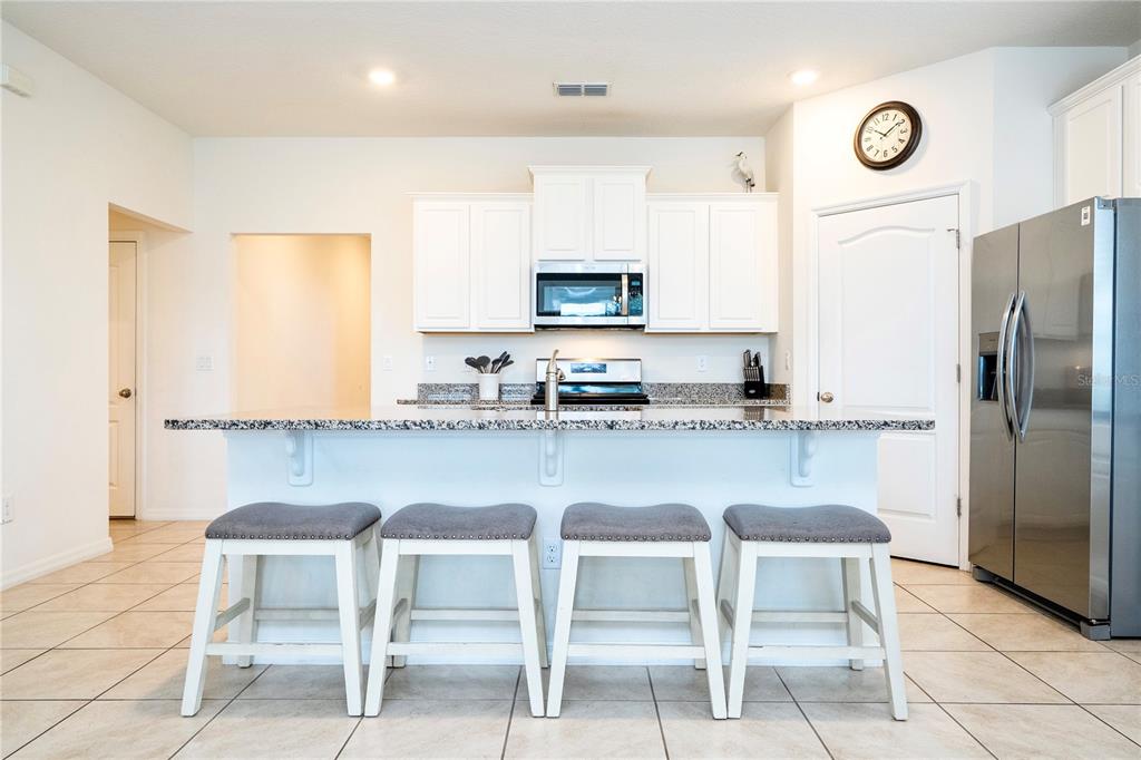 A kitchen features white cabinets, granite countertops, a center island with four stools, and tile flooring — 7560 OAKMOSS LOOP, DAVENPORT, FL
