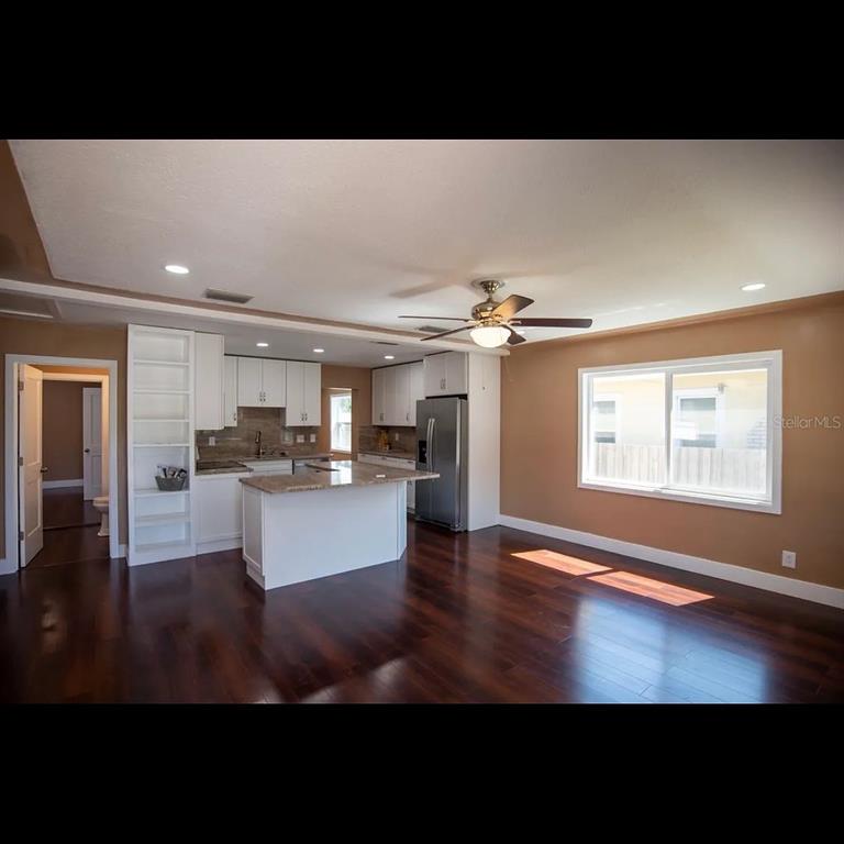 A kitchen with white cabinets, a granite island, and dark wood floors opens to a room — 1329 34TH AVENUE N, ST PETERSBURG, FL