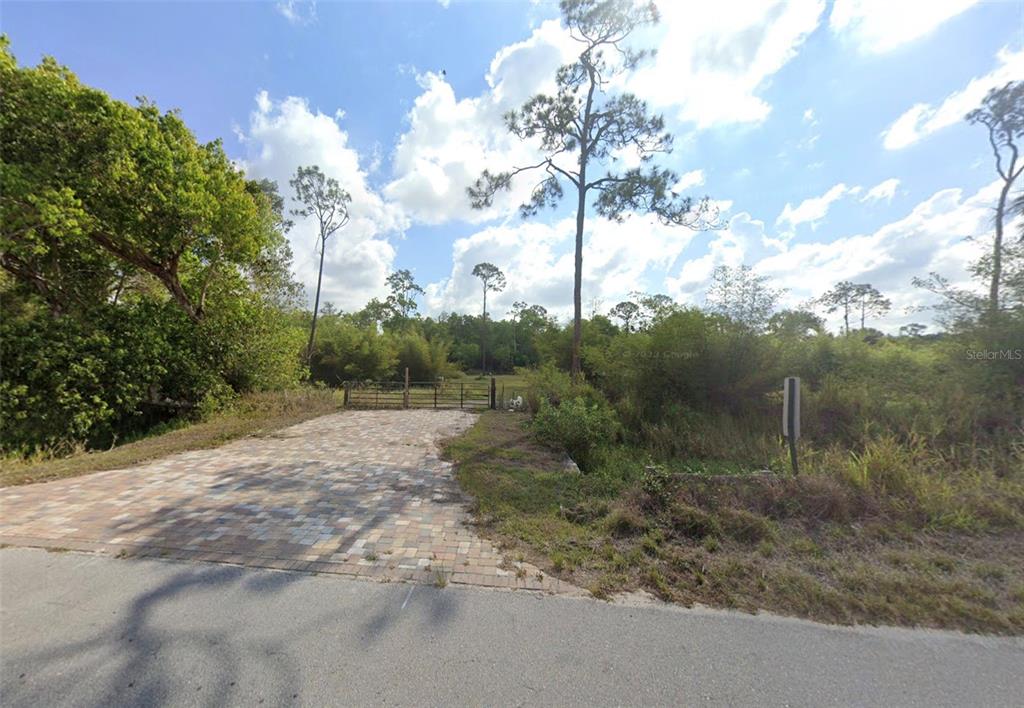 A paved driveway leads to a metal gate opening into a wooded, undeveloped lot — 11072 SIX LS FARM ROAD, NAPLES, FL