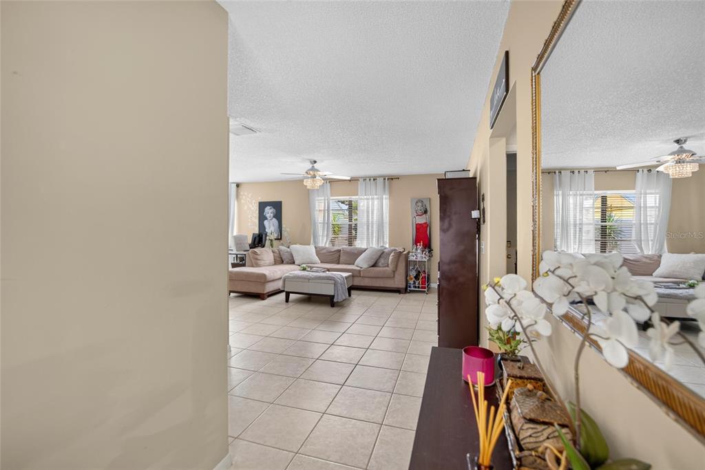 A view from a hallway into a living room with tile floors and a sectional sofa — 9063 DIXIANA VILLA CIRCLE, TAMPA, FL
