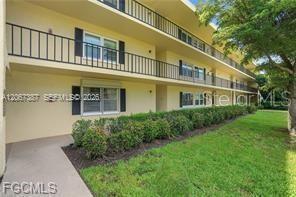 A three-story apartment building with a tan exterior, balconies, and surrounding landscaping — 1085 FOREST LAKES DRIVE UNIT 102, NAPLES, FL