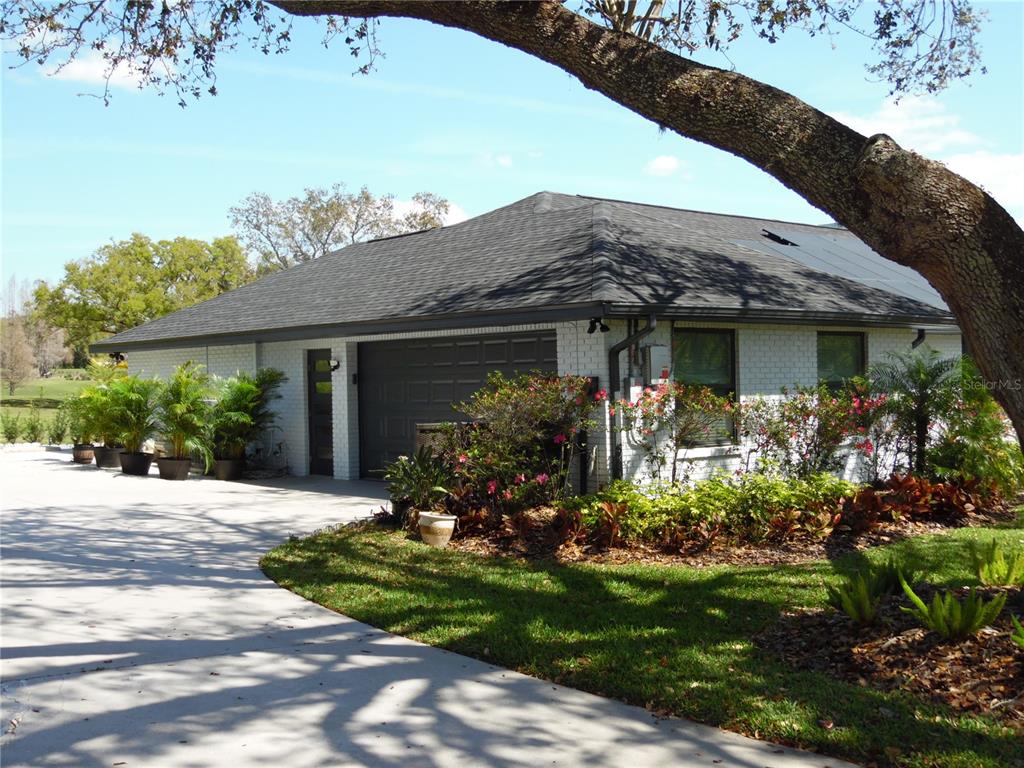 A white brick garage with a dark roof sits beside a paved driveway under trees — 2709 FAIRWAY VIEW DRIVE, VALRICO, FL
