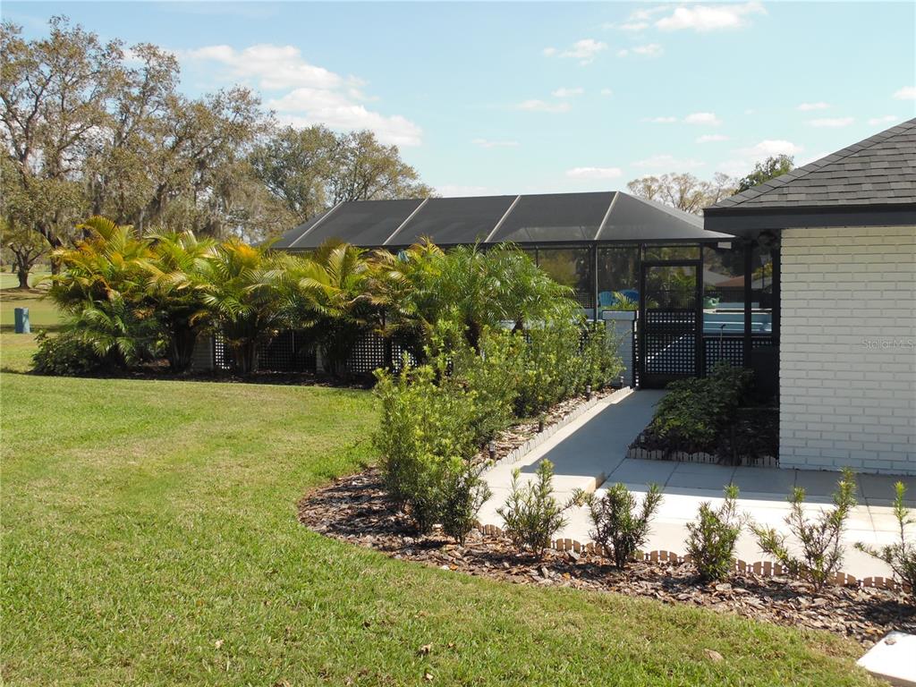 A white brick house exterior features a screened-in pool enclosure and landscaped garden beds — 2709 FAIRWAY VIEW DRIVE, VALRICO, FL