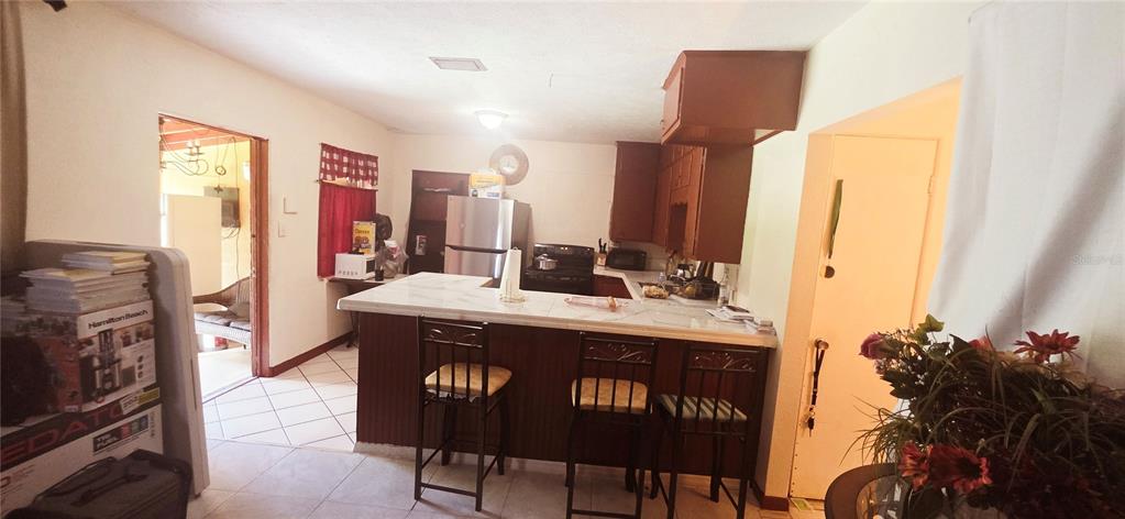 A kitchen features a breakfast bar with three stools, wooden cabinets, and tile flooring — 1135 HOLDEN AVENUE UNIT 1/2, ORLANDO, FL
