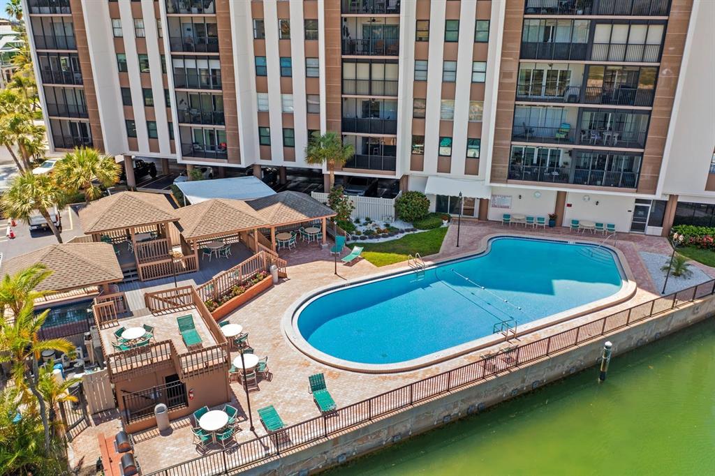 An aerial view of a swimming pool and patio area next to a multi-story building — 10355 PARADISE BOULEVARD UNIT 512, TREASURE ISLAND, FL