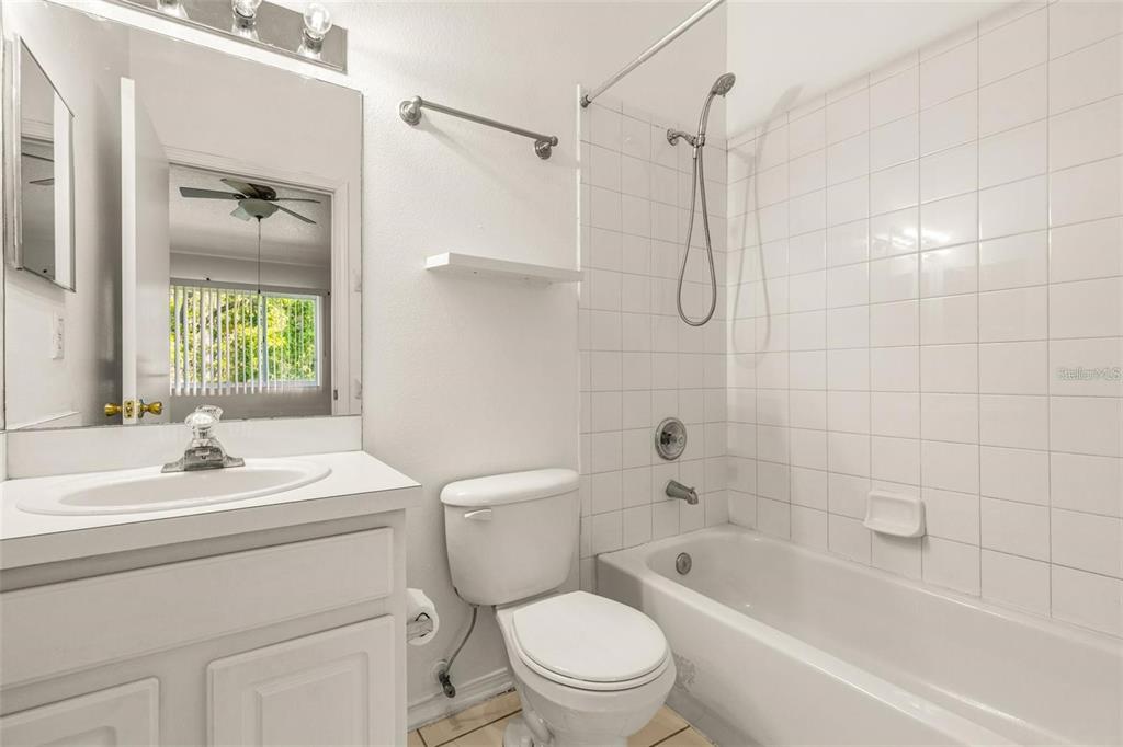 A bathroom features a white vanity, a toilet, and a shower-tub combination with white tiles — 1237 KENNEWICK COURT, WESLEY CHAPEL, FL
