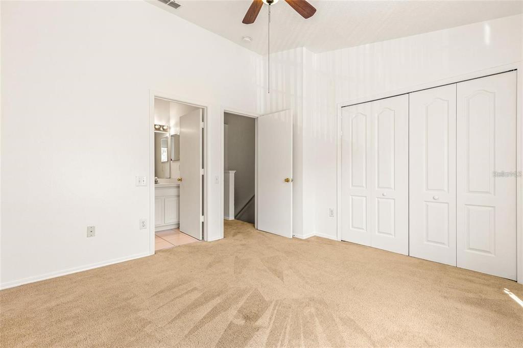 A bedroom with beige carpet, white walls, a ceiling fan, and two white closet doors — 1237 KENNEWICK COURT, WESLEY CHAPEL, FL